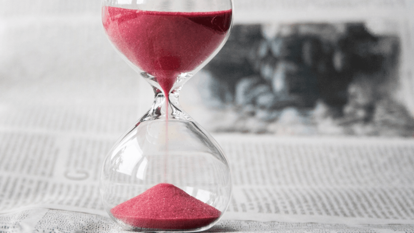 hour glass with red sand on newspaper