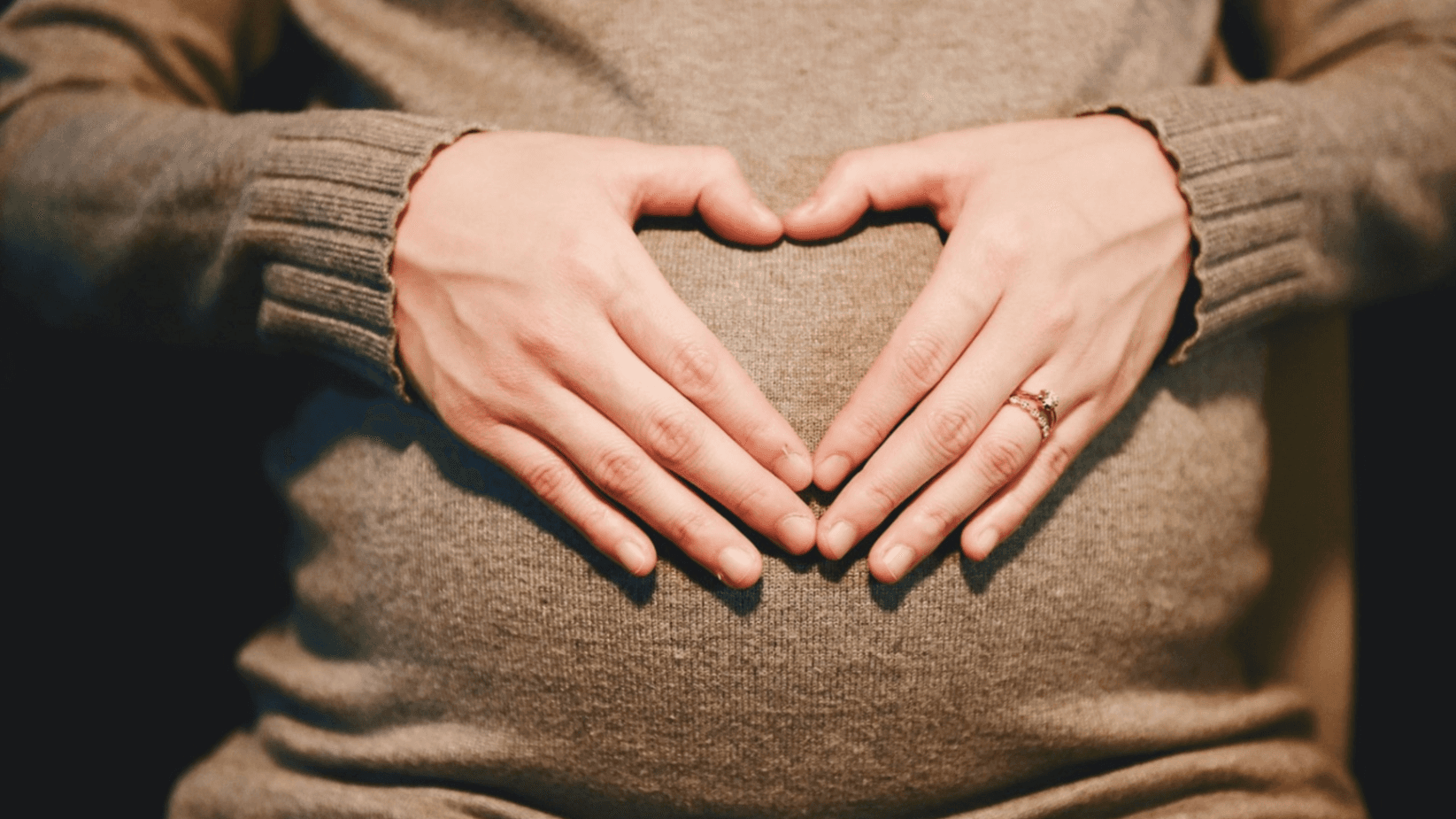 pregnant woman with heart hands over stomach